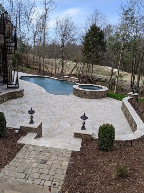 Travertine pool deck with a spa and stone walls